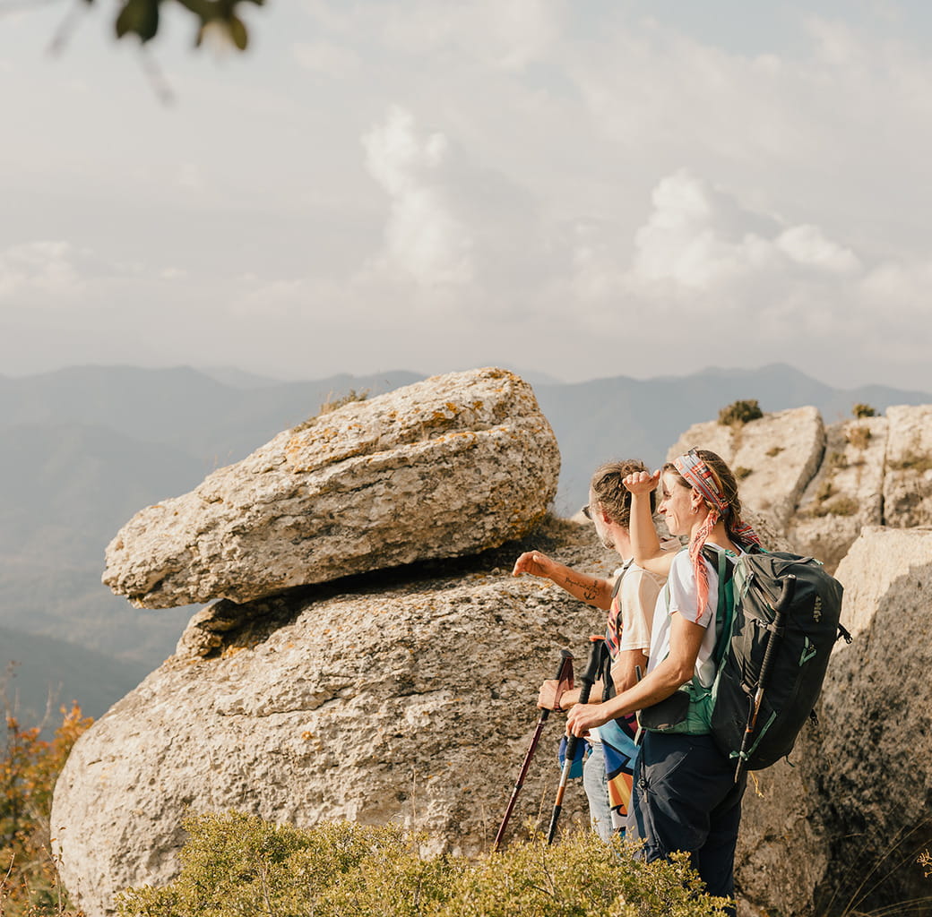 Two people standing next to a large rock look out at the view