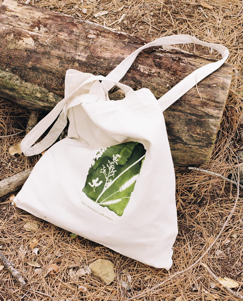 A canvas bag with printed leaf symbol rests against a log on the ground
